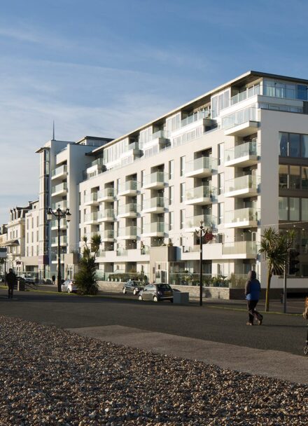 Hotel building with balconies and windows facing the sea front promenade with people walking along