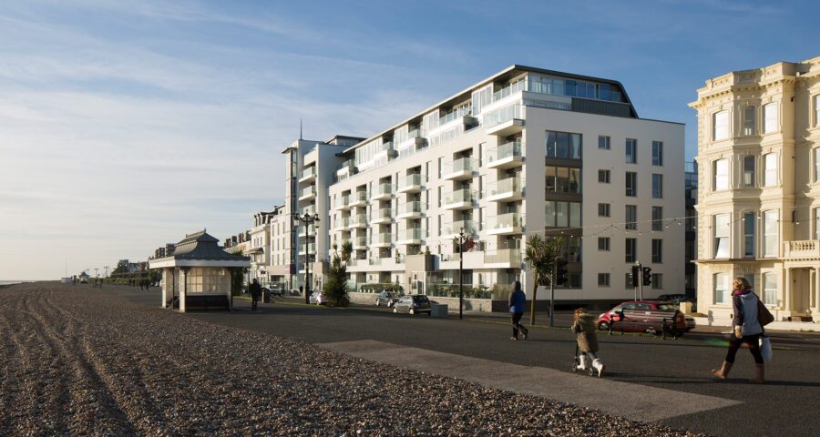 Hotel building with balconies and windows facing the sea front promenade with people walking along
