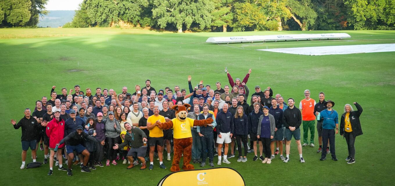 Group of people standing on a cricket ground, cheering and looking at the camera.