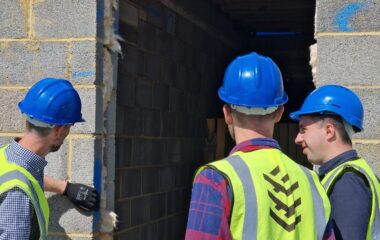 Three men wearing hard hats looking at a newly built wall.