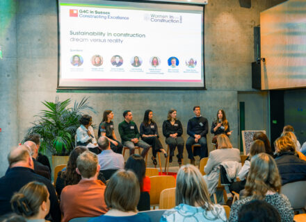 Seven people sitting on stools at the front of a stage, looking at the audience.