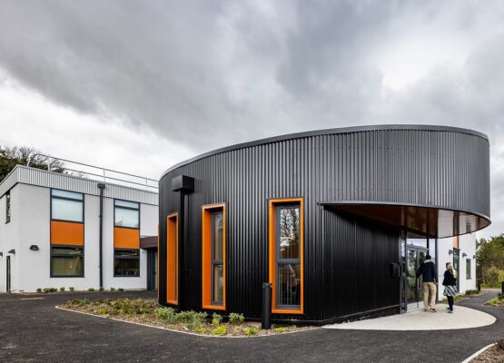 Large office entrance exterior clad in black metal, with orange window frames and a white extension to the back,
